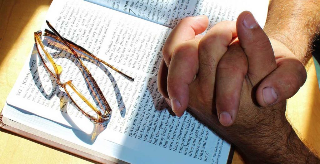 Hands praying over open Bible