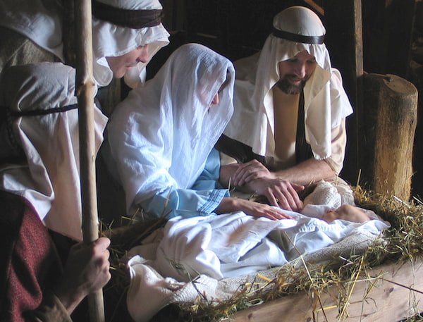 Mary and Joseph and a shepherd look lovingly at Jesus in the manger
