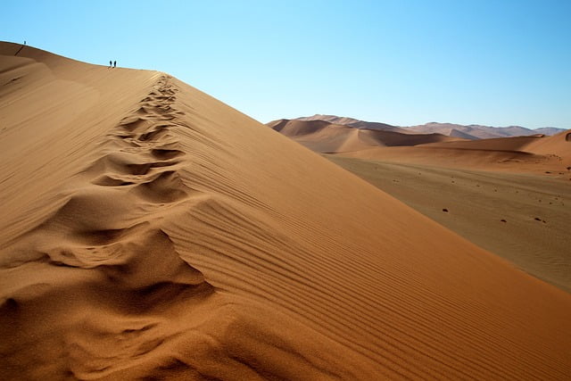Sand dune in Namibian desert with two walkers on the crest